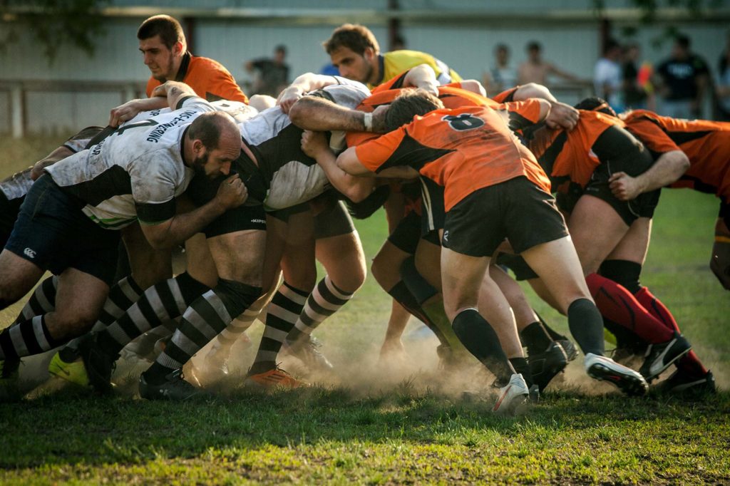Two sets of rugby teams are pushing against each for control of the ball