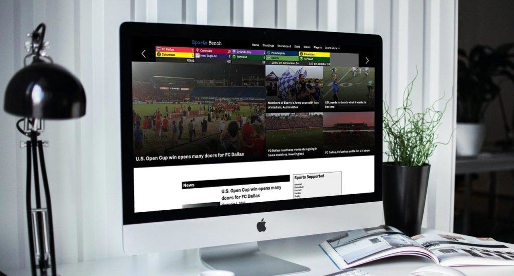 An Apple iMac showing the Sports Bench Soccer homepage on a white desk in a white room