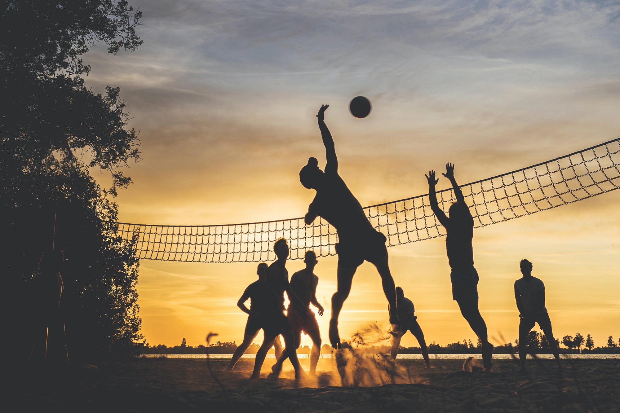 Group of friends playing beach volleyball as the sun is setting.